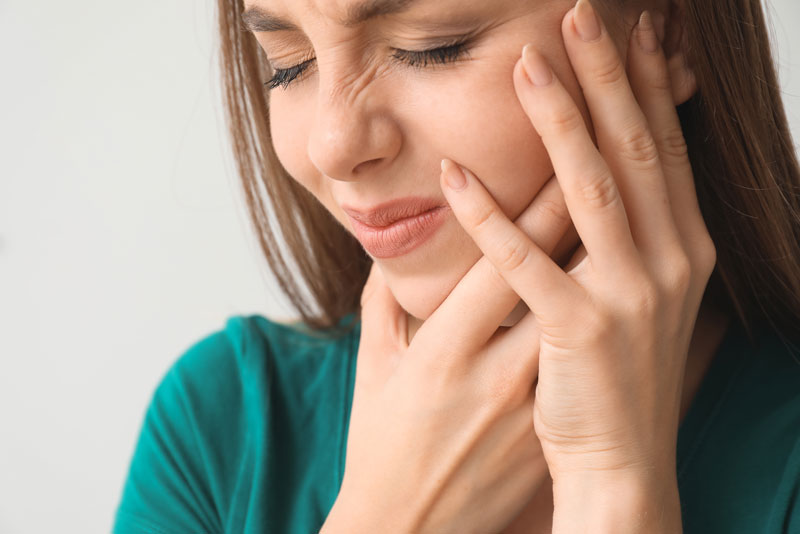 a patient holding her jaw and cheek in pain while she is waiting for the doctor to correct her dental implants that have failed.