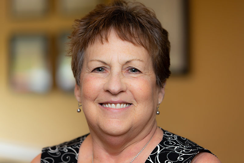 Smiling woman with short brown hair wearing a black blouse with a white pattern.